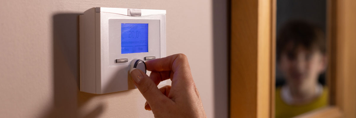 A picture of a woman adjusting a thermostat as a child watches
