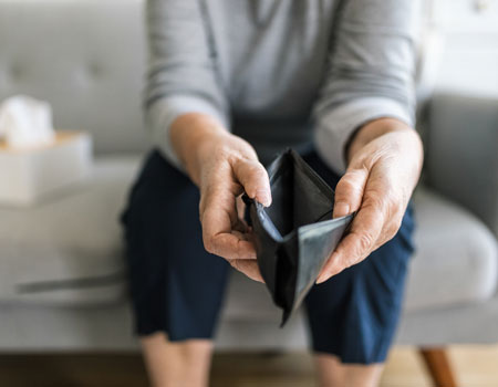A picture of an older person sitting on a couch holding open an empty wallet